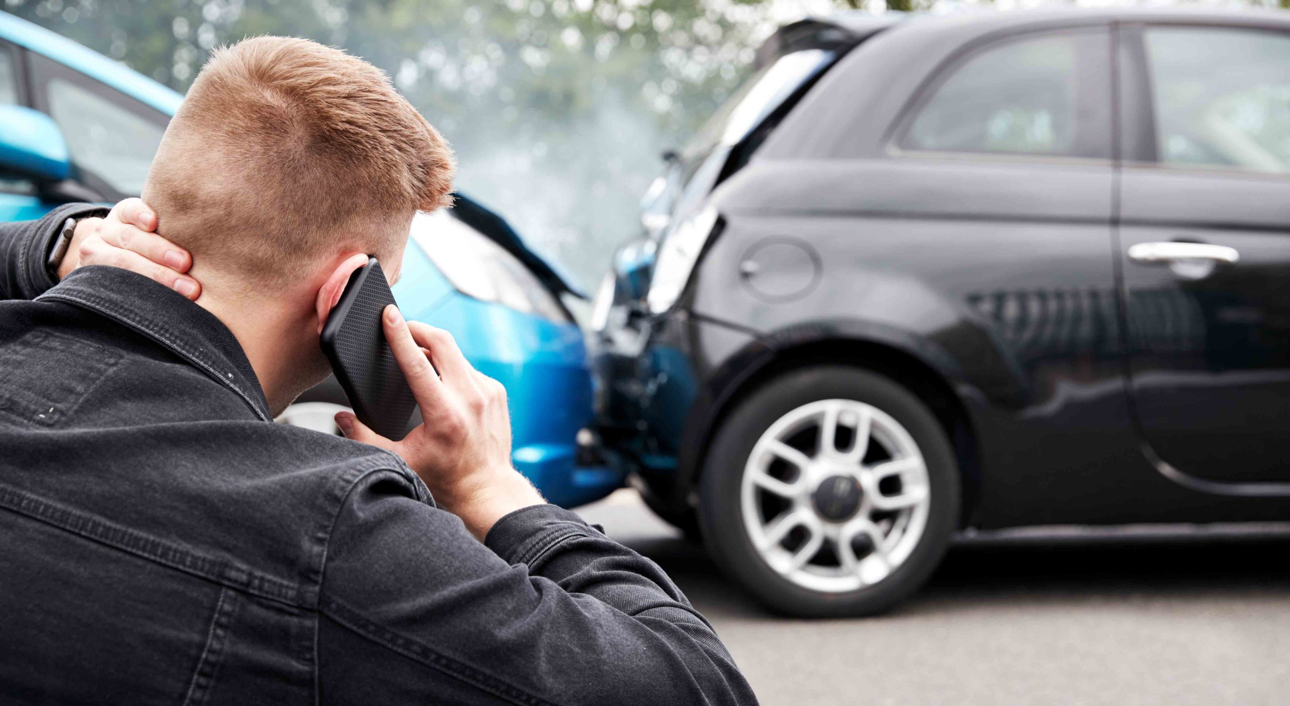 Man on phone holding his neck after a rear-end car accident involving two vehicles with visible damage