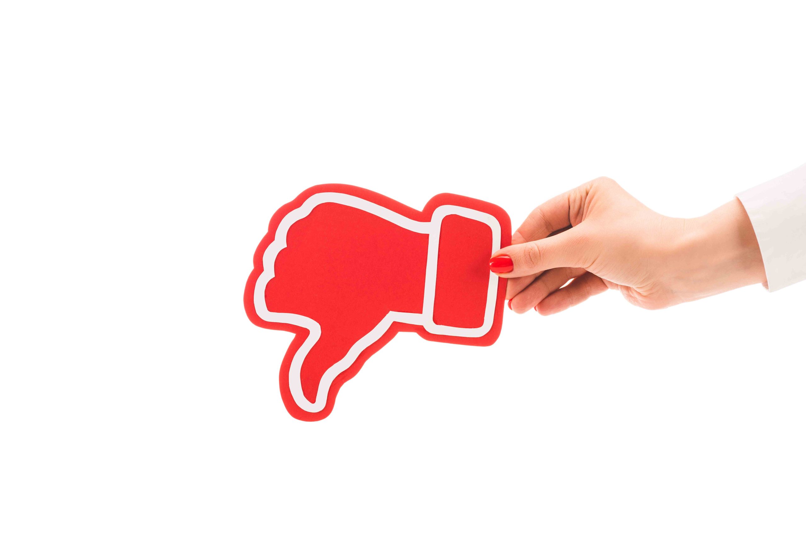 Hand holding a red thumbs down symbol on a white background, signifying avoidance of posting car accidents on social media.