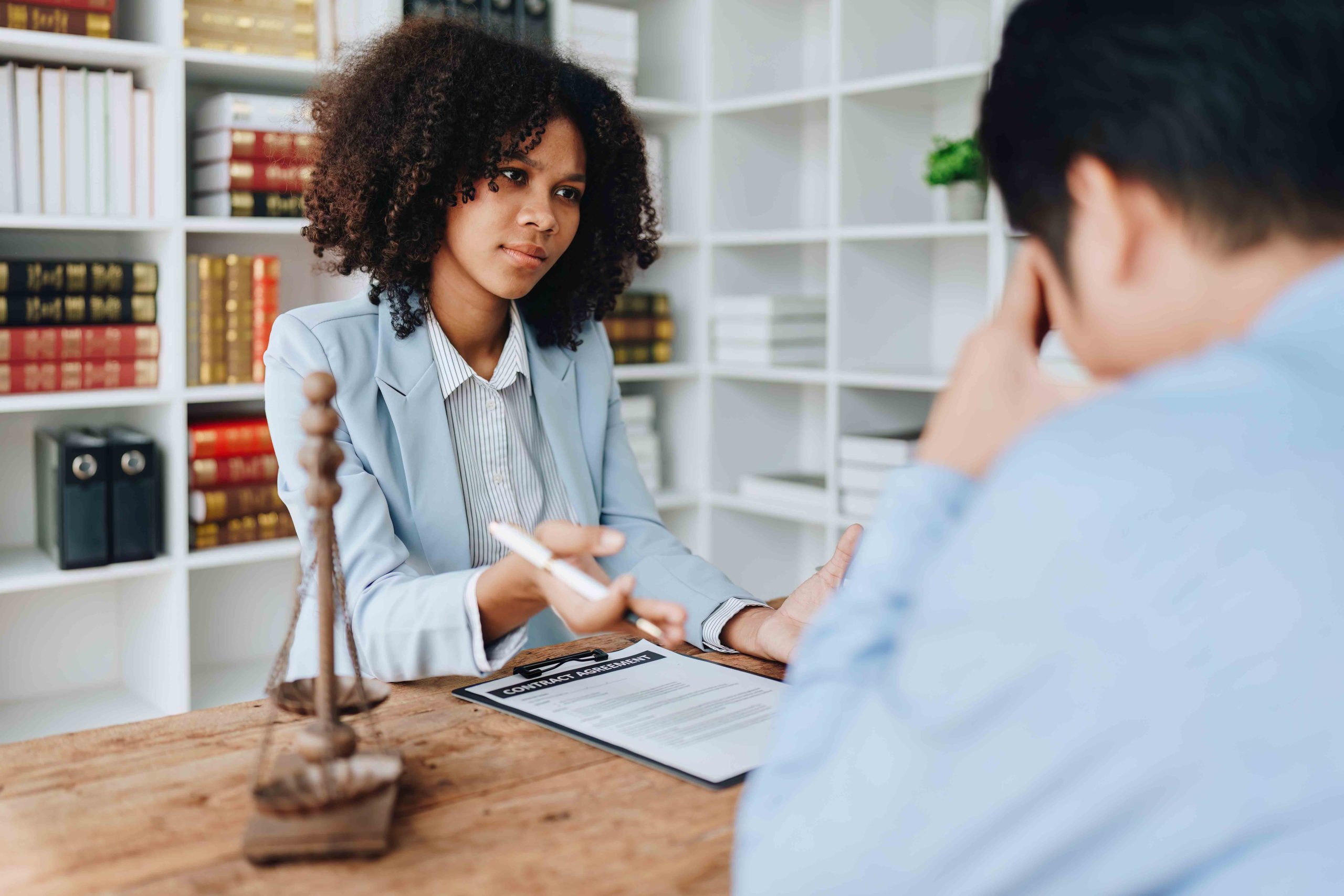 Car accident lawyer discussing a legal document with a stressed client in an office, with scales of justice in the foreground.