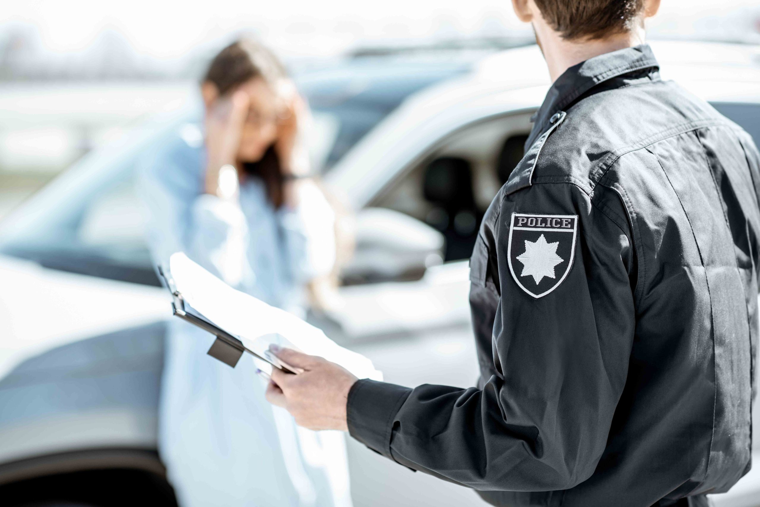 Police officer taking notes while a distressed woman stands near a car after an accident. 