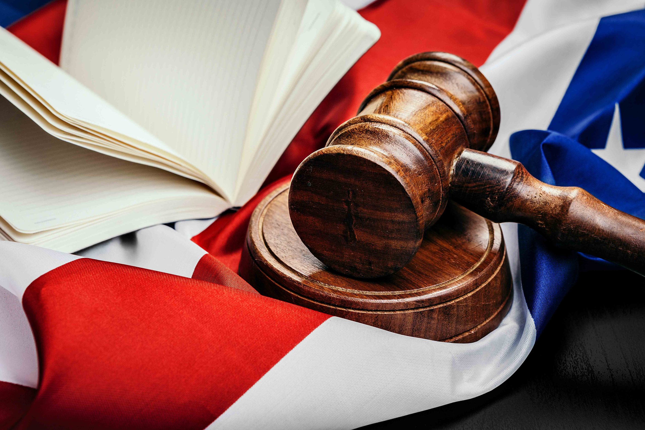 Wooden gavel and open book on the American flag, symbolizing justice and law in the USA.