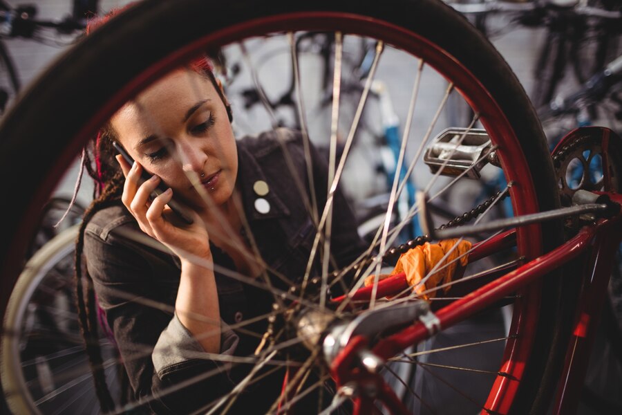 Person calling their insurance company while standing next to a damaged bicycle in a bicycle shop after an accident