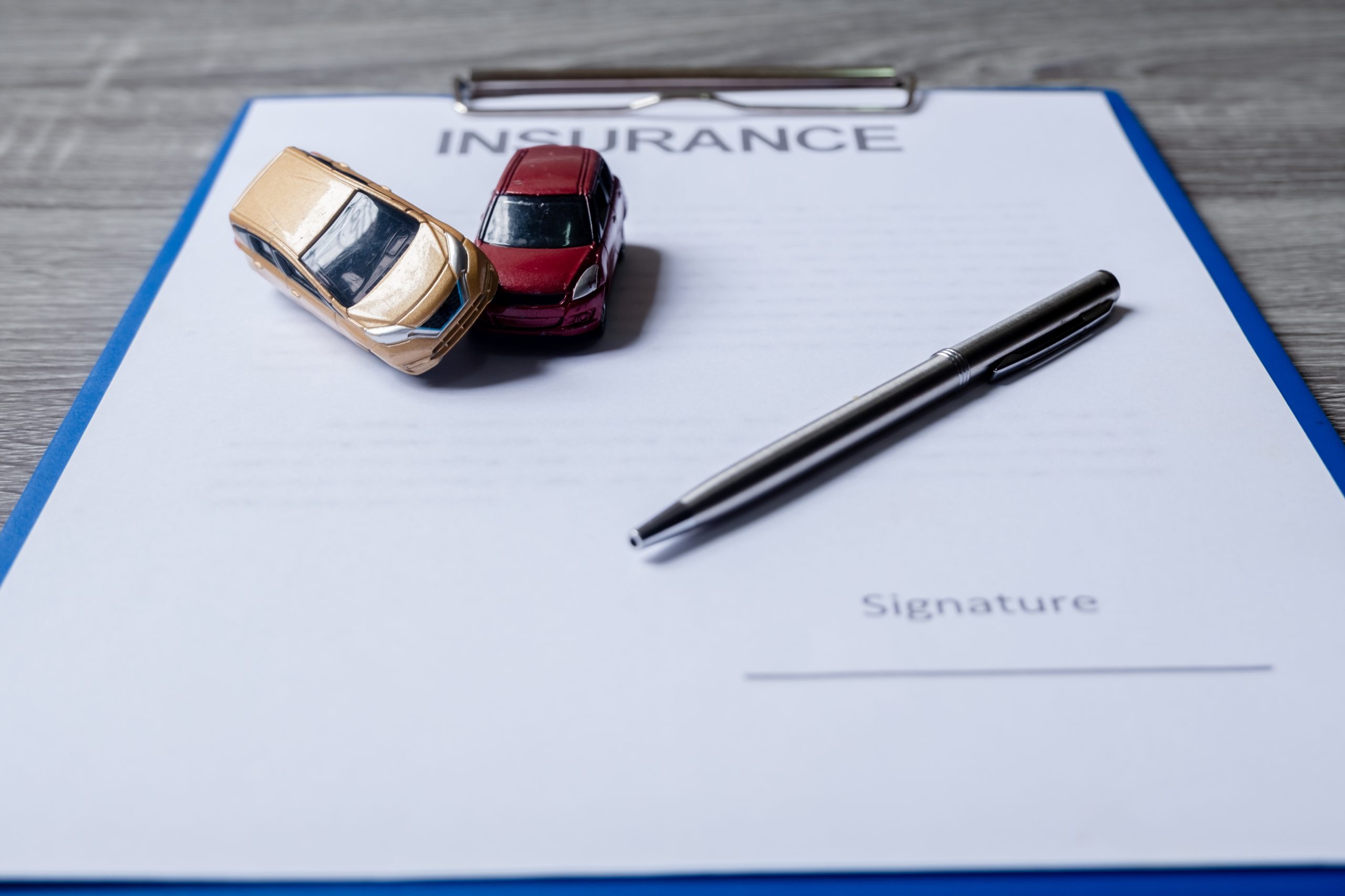 A car insurance document with toy cars and a pen on top, symbolizing an insurance claim process.