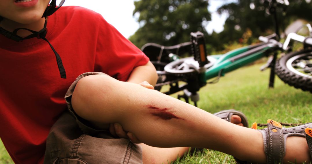 Young boy with scraped shin sitting on the ground after a bicycle accident, bike in the background