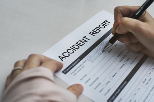 Close-up of an injured person's hand holding a pen and filling out an accident report form due to hit-and-run