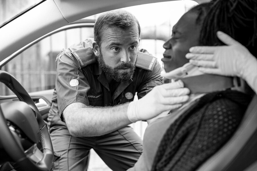 A paramedic carefully placing a cervical collar on an injured woman inside a car after an accident, ensuring her safety