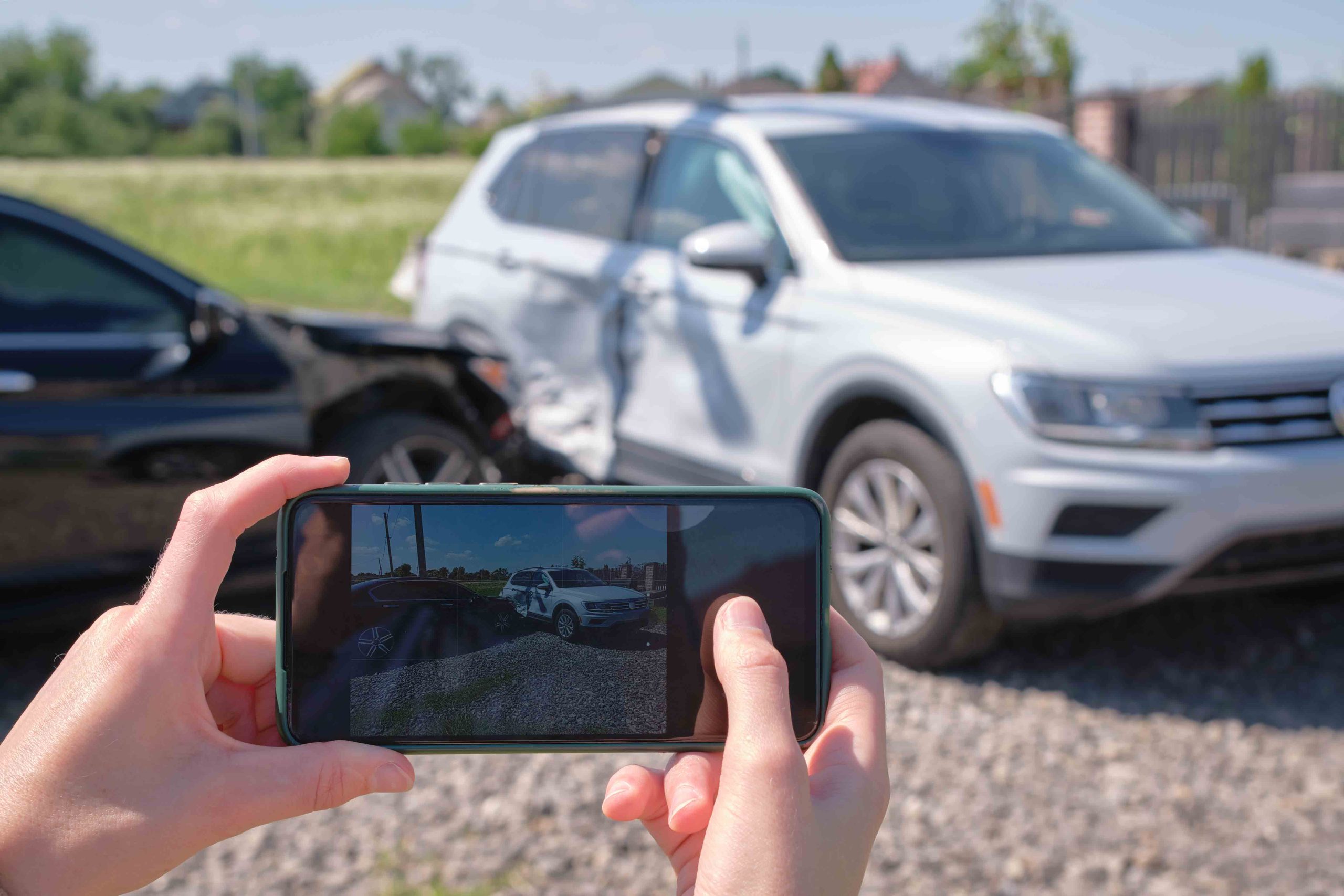 Woman taking photos of car accident damage on her phone, documenting the collision scene. 