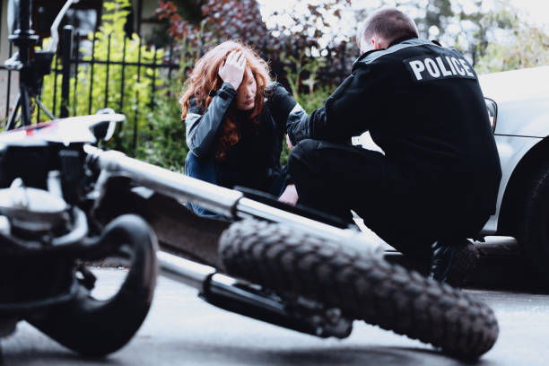 Close-up of a wrecked motorcycle on a paved road surrounded by broken glass and debris after an accident
