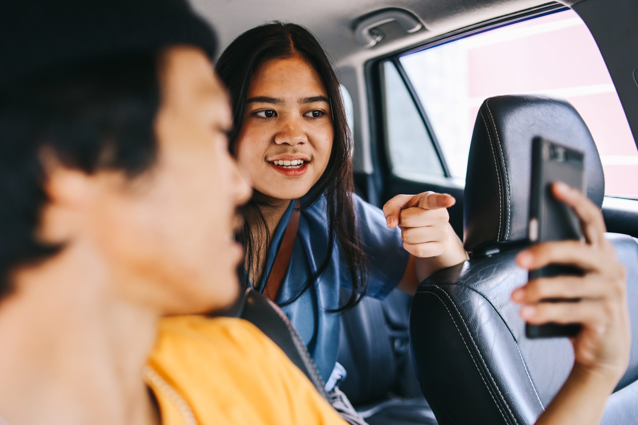 A passenger interacting with an Uber driver inside a car, pointing at a smartphone