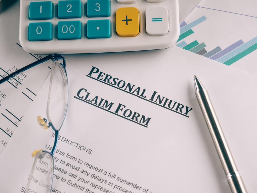 A personal injury claim form with glasses, a pen, and a calculator on top, emphasizing the process of filing for compensation after an accident.