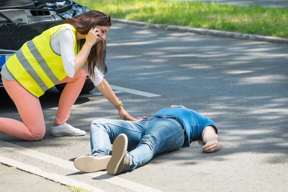 Crossing guard assisting an injured person lying on the road after a pedestrian accident, emphasizing the need for immediate medical attention