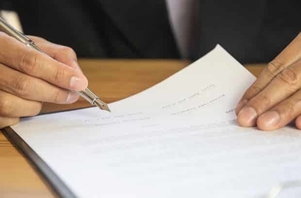 Close-up of hands signing an insurance claim form, highlighting the importance of filing claims after an accident to seek compensation for damages