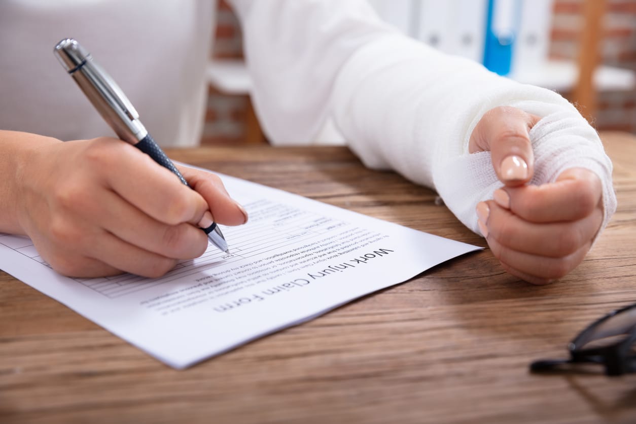 Close-up of a person filling out a workplace injury claim form, illustrating the importance of filing workers' compensation claims promptly