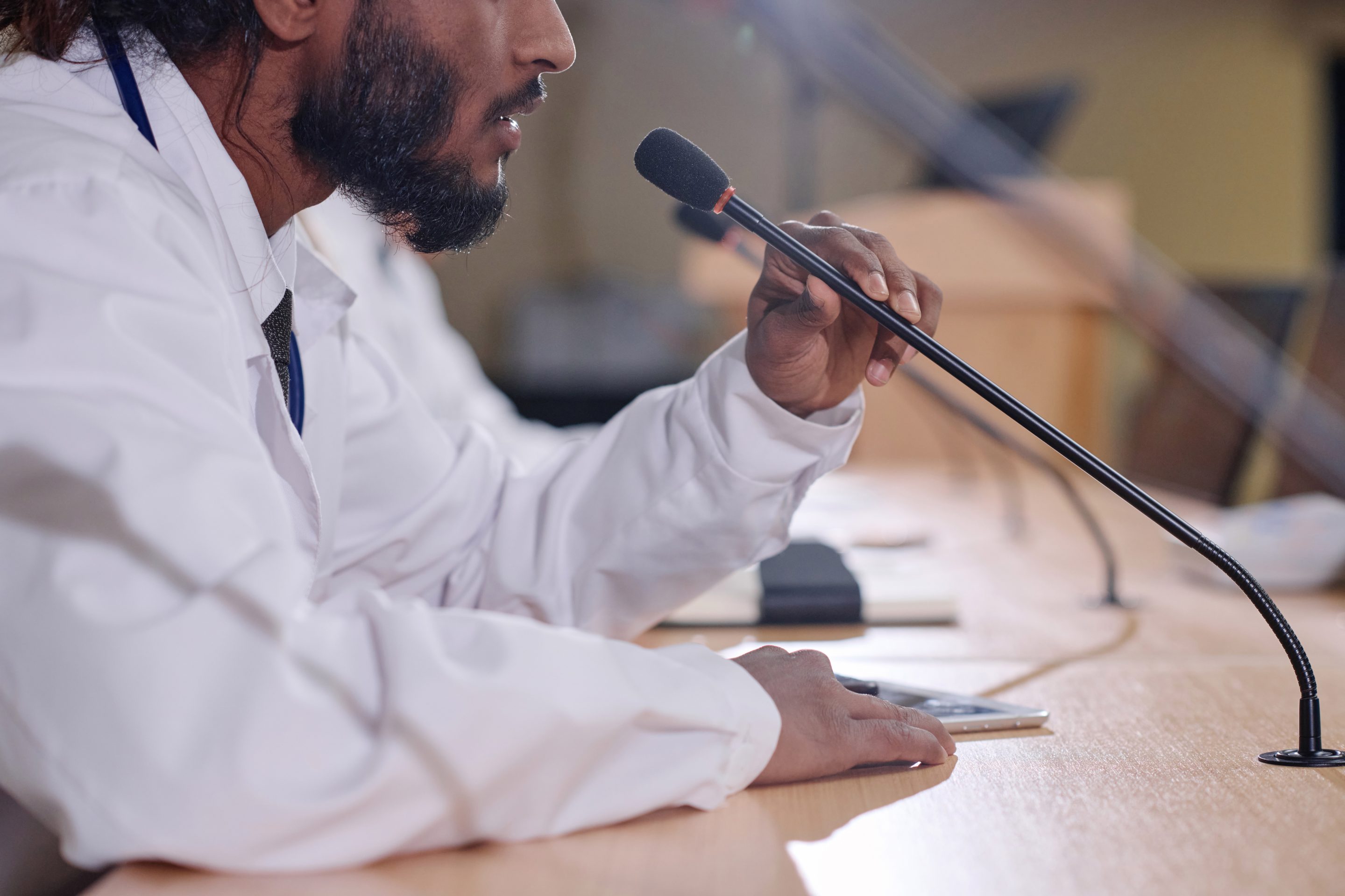 A person in a white lab coat speaking into a microphone at a desk with papers, signifying the importance of expert witnesses in personal injury cases