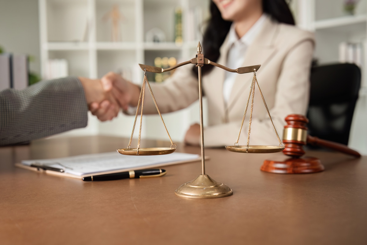 A woman and a man shake hands in a parking lot, with the man holding a scale, indicating a resolution after a car accident