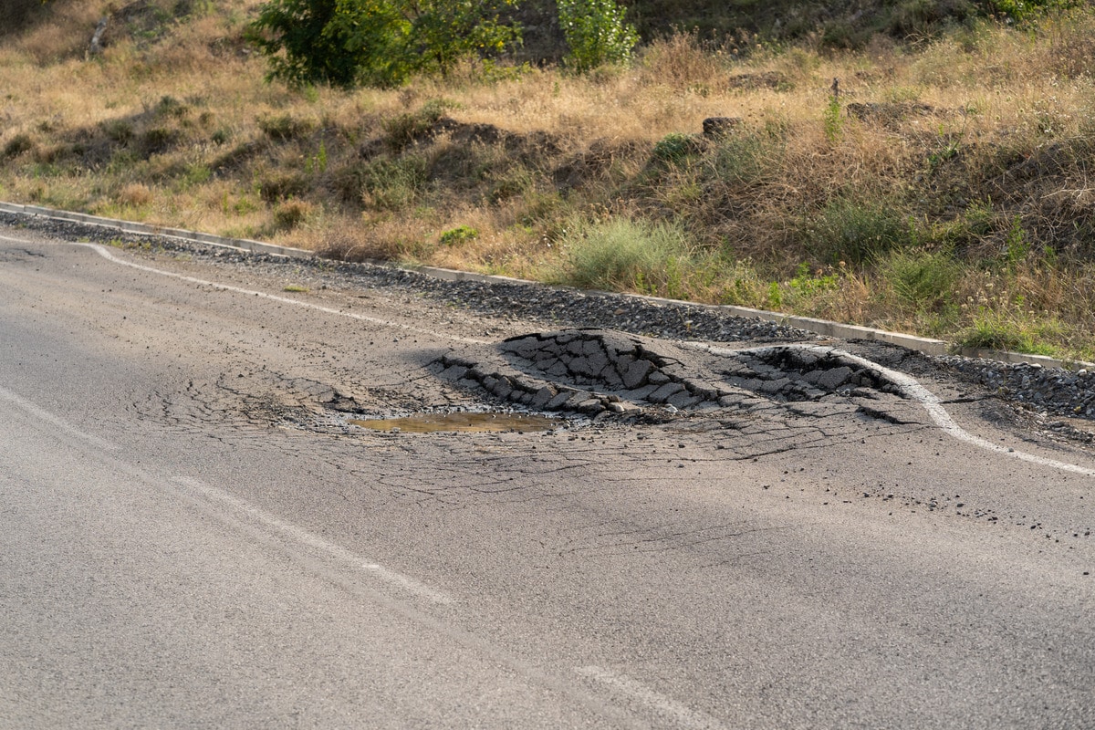 A deep pothole on the roadside, highlighting poor road conditions that may lead to car accidents