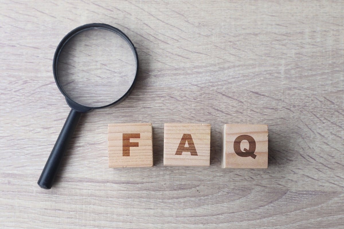 Wooden blocks spelling "FAQ" beside a magnifying glass on a table