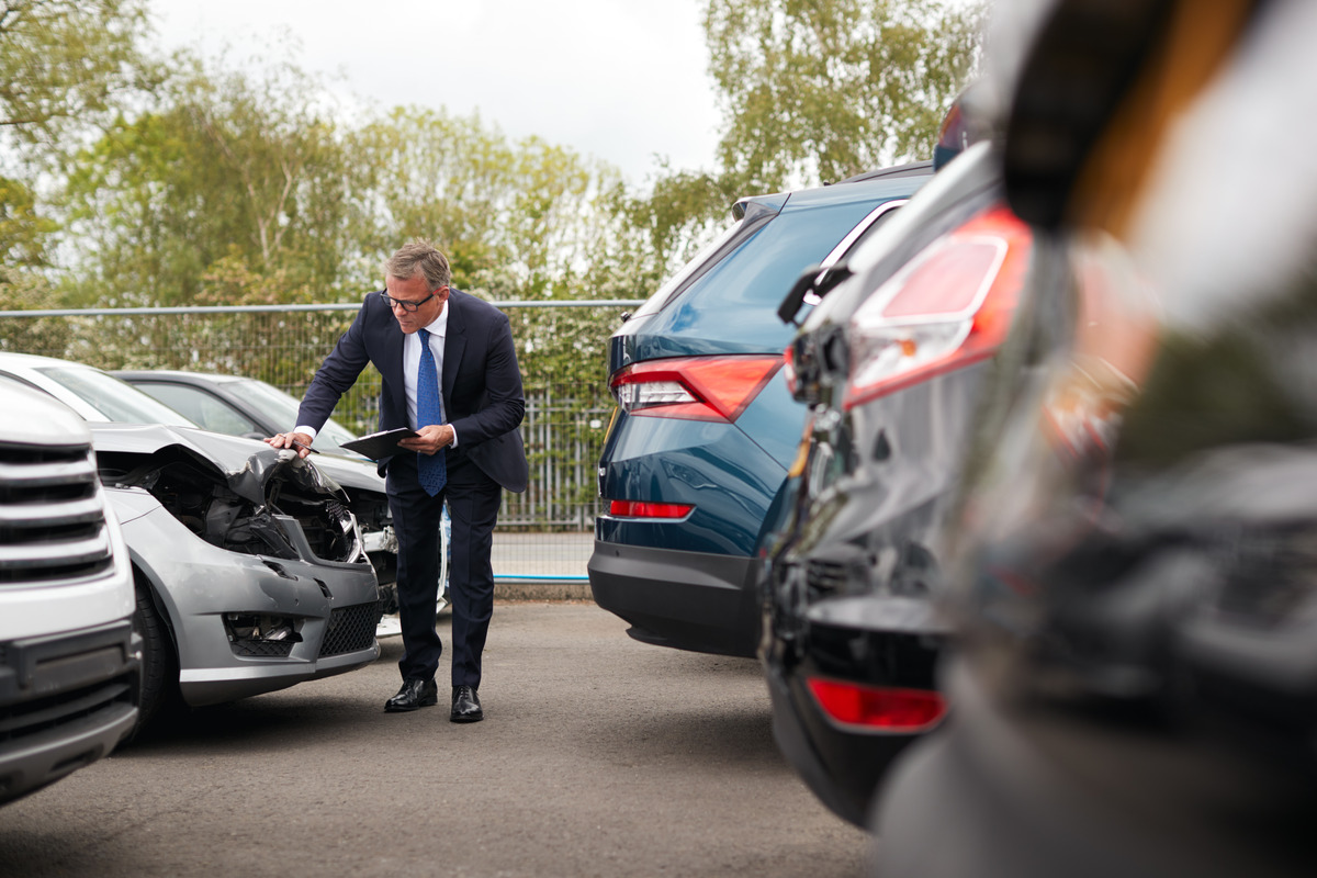 A man in a suit examines a damaged car in a parking lot following a car accident