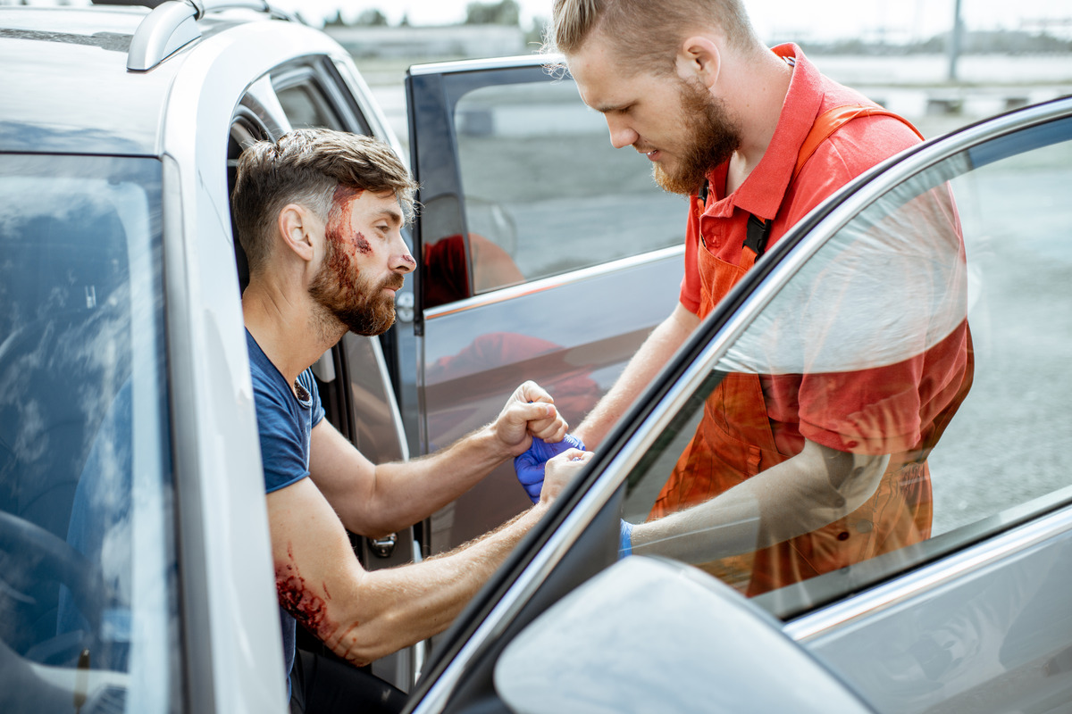 A man assists another man by opening his car door in a parking lot following a car accident