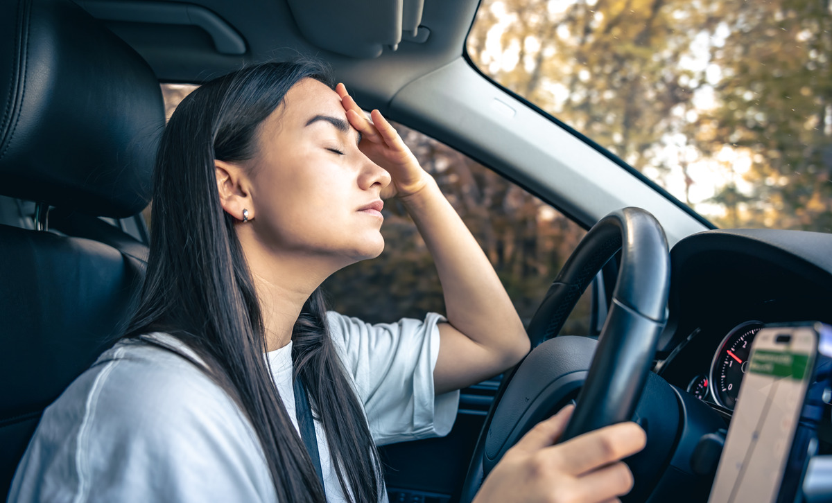 A woman sits in her car, holding her head, visibly distressed after a car accident in a parking lot