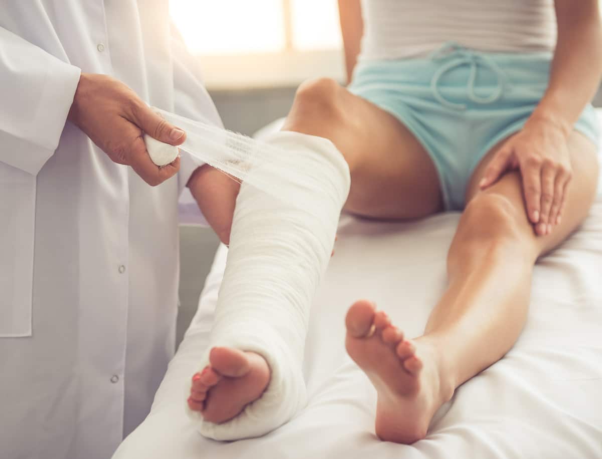 Doctor wrapping patient’s leg with a medical cast during treatment
