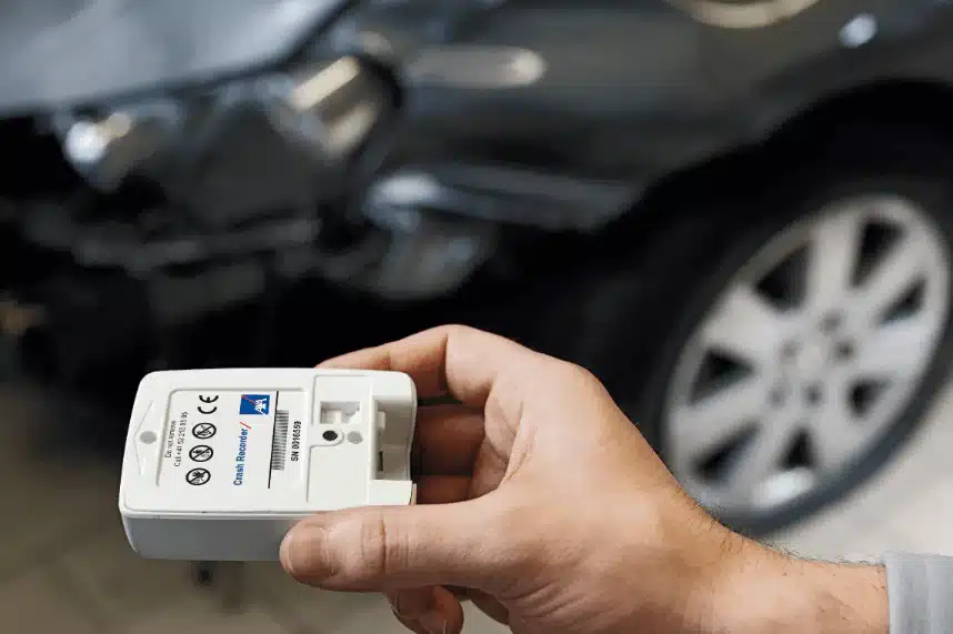 Man holding a crash recorder with a wrecked car in the backgroun