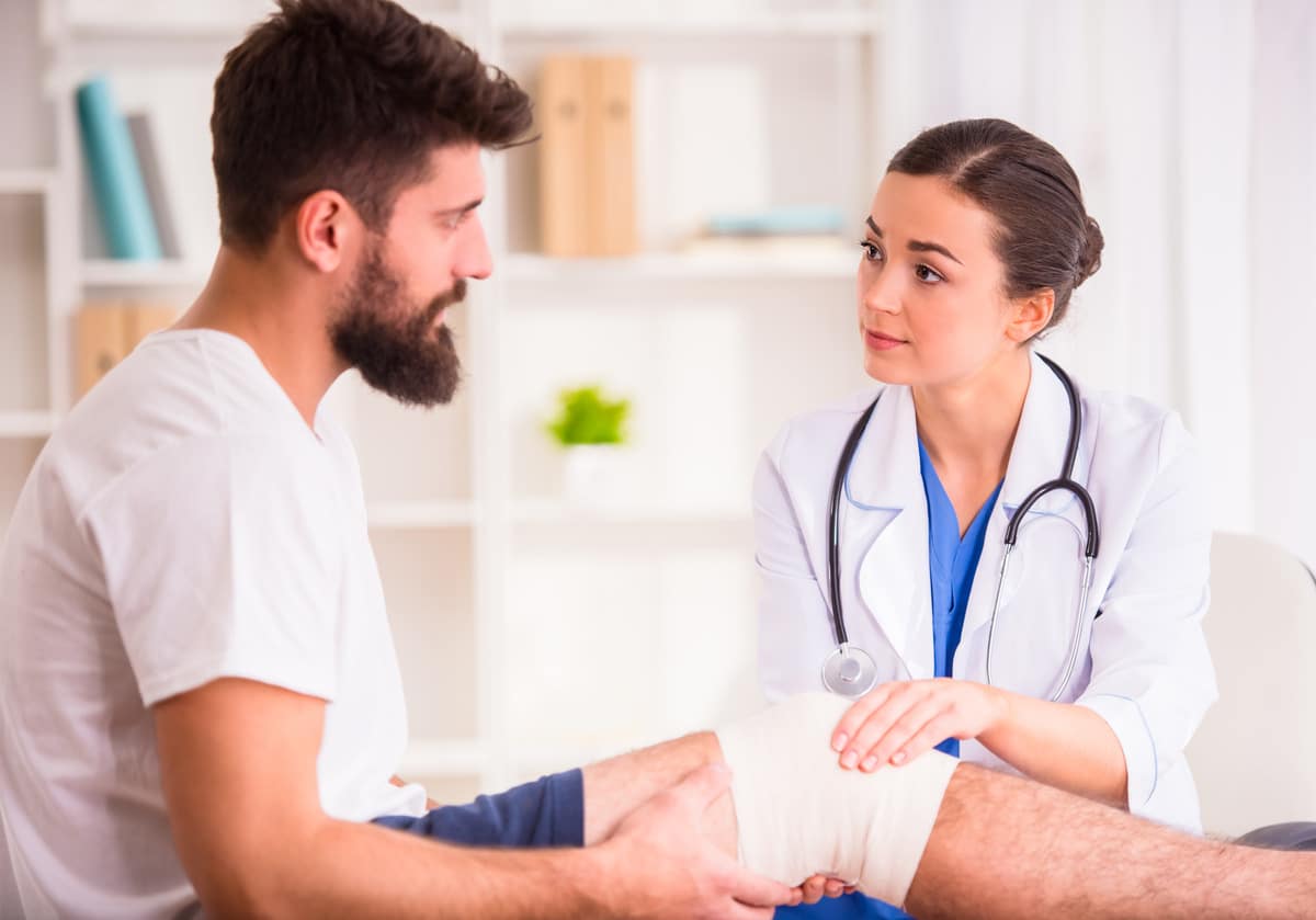 Doctor checking up on a man bandaged on its knee