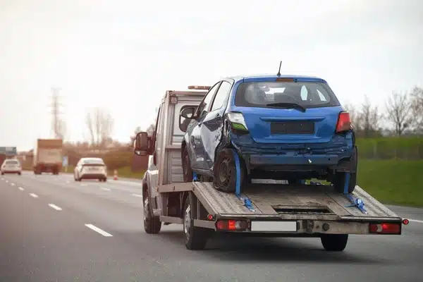 tow truck driving on the road while carrying a damaged blue car