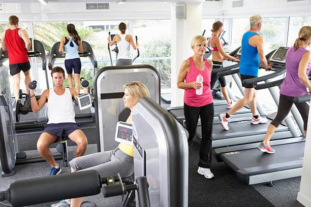 Crowded gym floor with many people exercising and using machines simultaneously