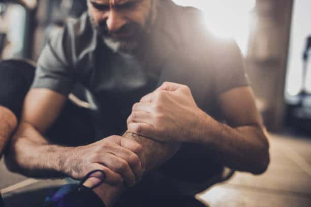 Man suffering leg injury at the gym while holding his ankle in pain