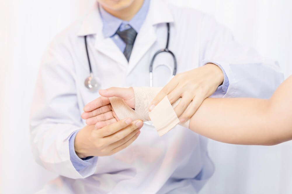 Close-up of a doctor in a white coat and stethoscope applying a compression bandage or wrap to a patient's injured wrist or forearm