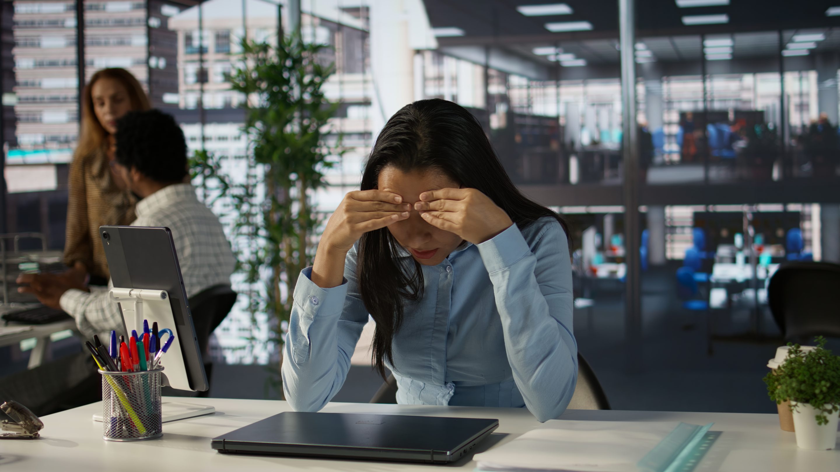Stressed, overwhelmed female office worker with her head in her hands experiencing professional burnout at her desk