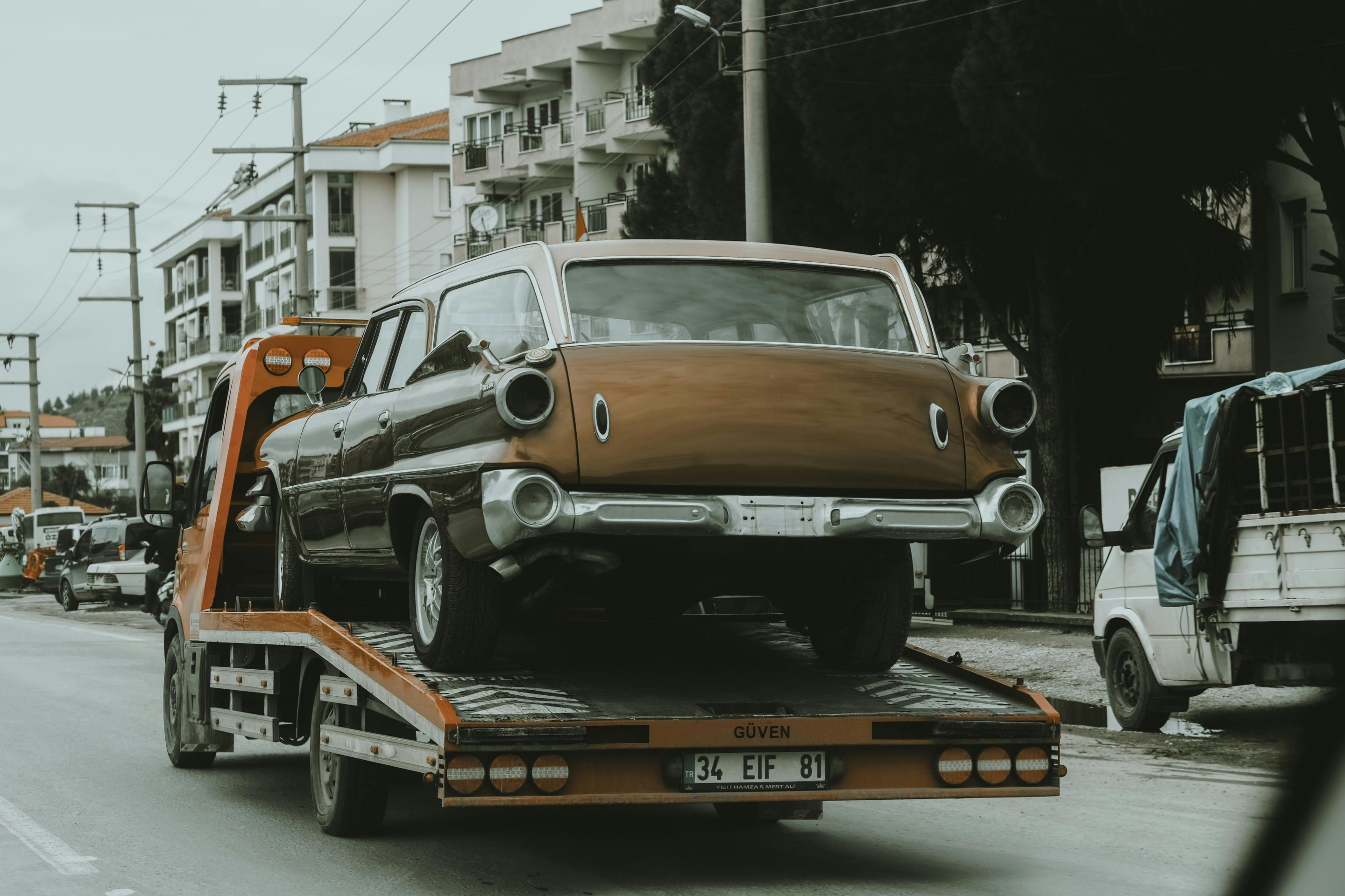 tow truck driving on the road while carrying a damaged blue car