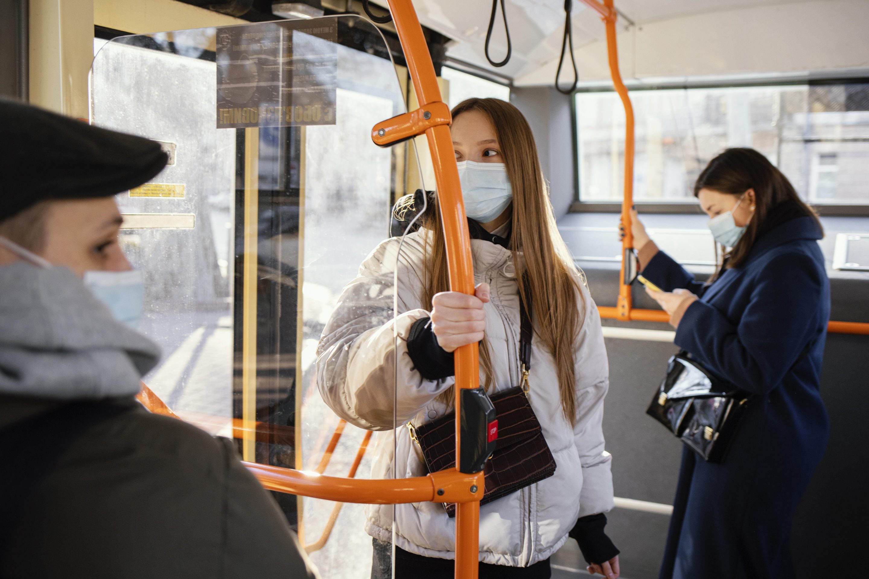 Commuters wearing face masks while standing on a public bus and holding handrails